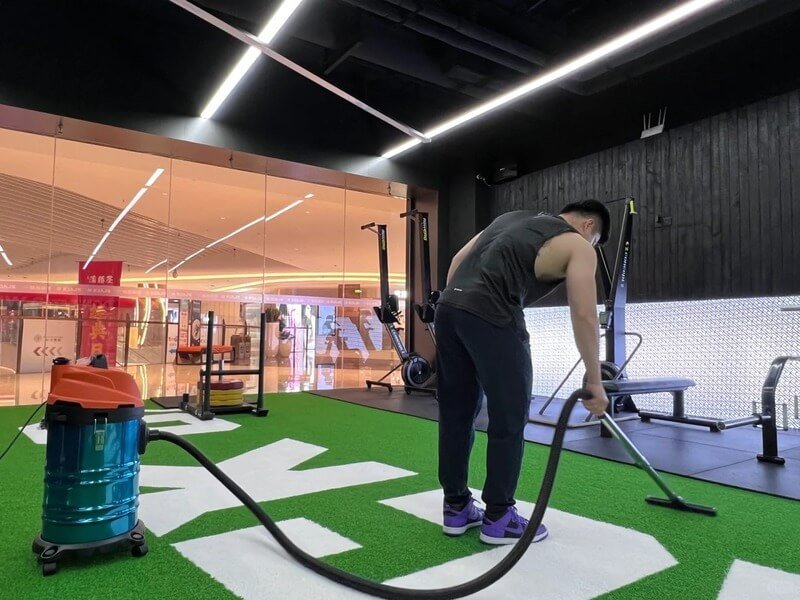 Cross-section view of padded gym turf showing the green nylon fibers bonded to a thick black closed-cell foam backing.